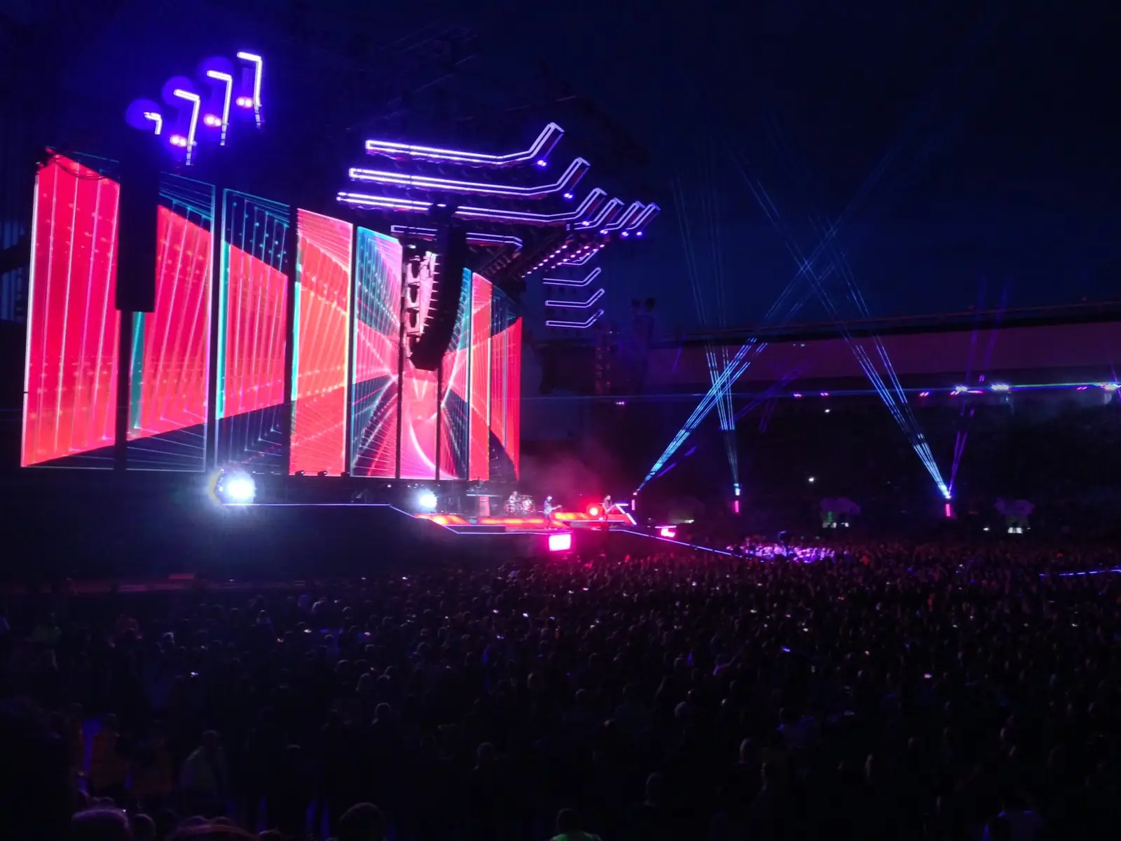 Estádio lotado com palco iluminado em roxo durante um show à noite